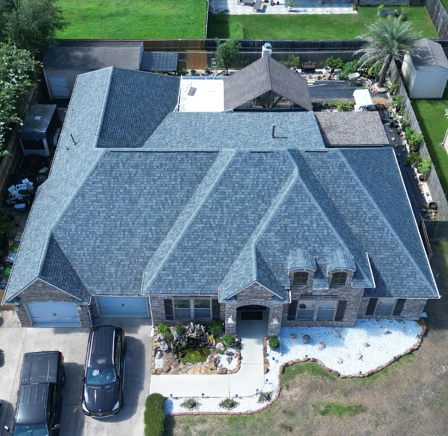Aerial view of a finished gray shingle roof on a brick home with a stone garden entry