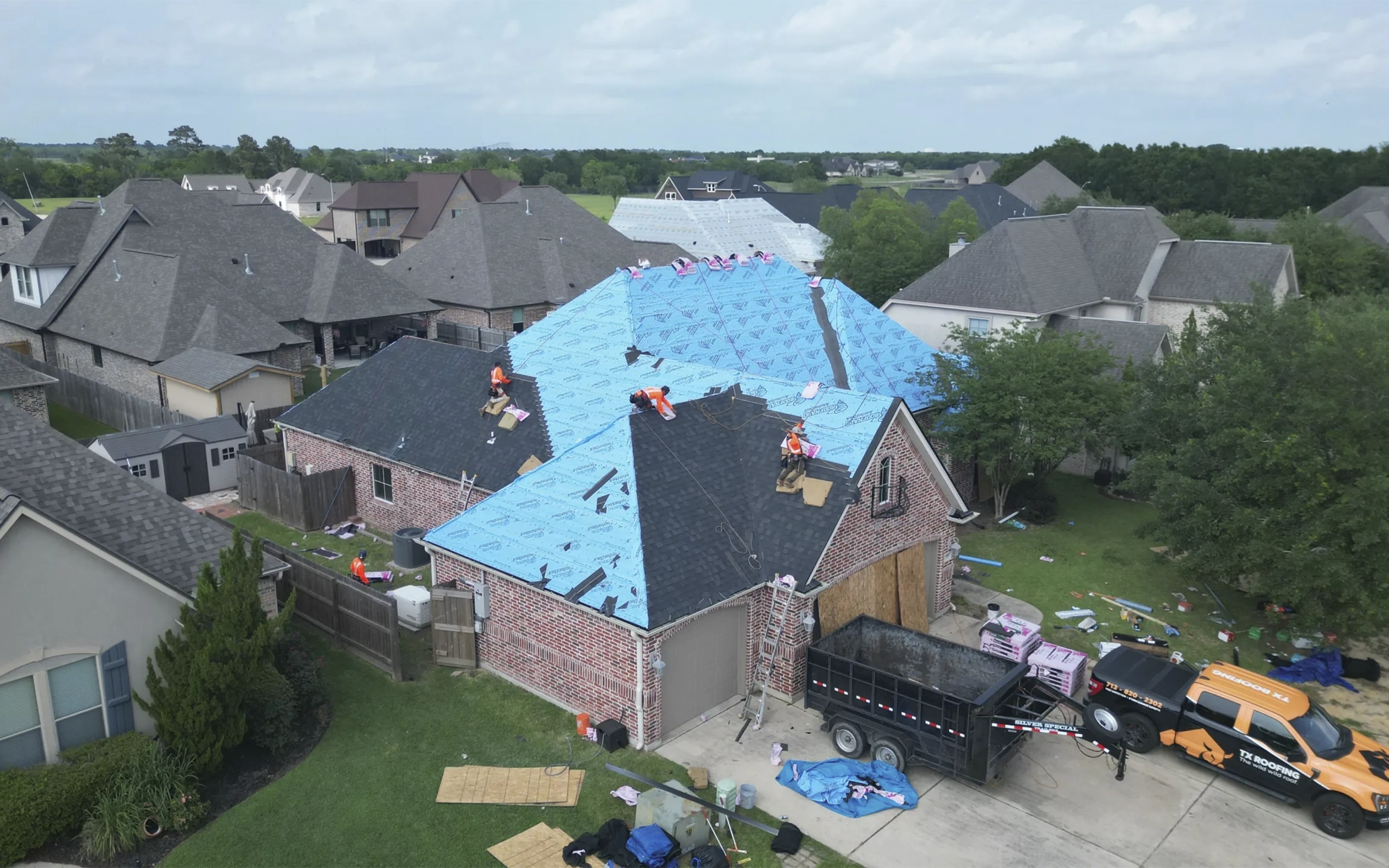 Aerial view of a roof replacement in progress with the TX Roofing truck and trailer in the driveway