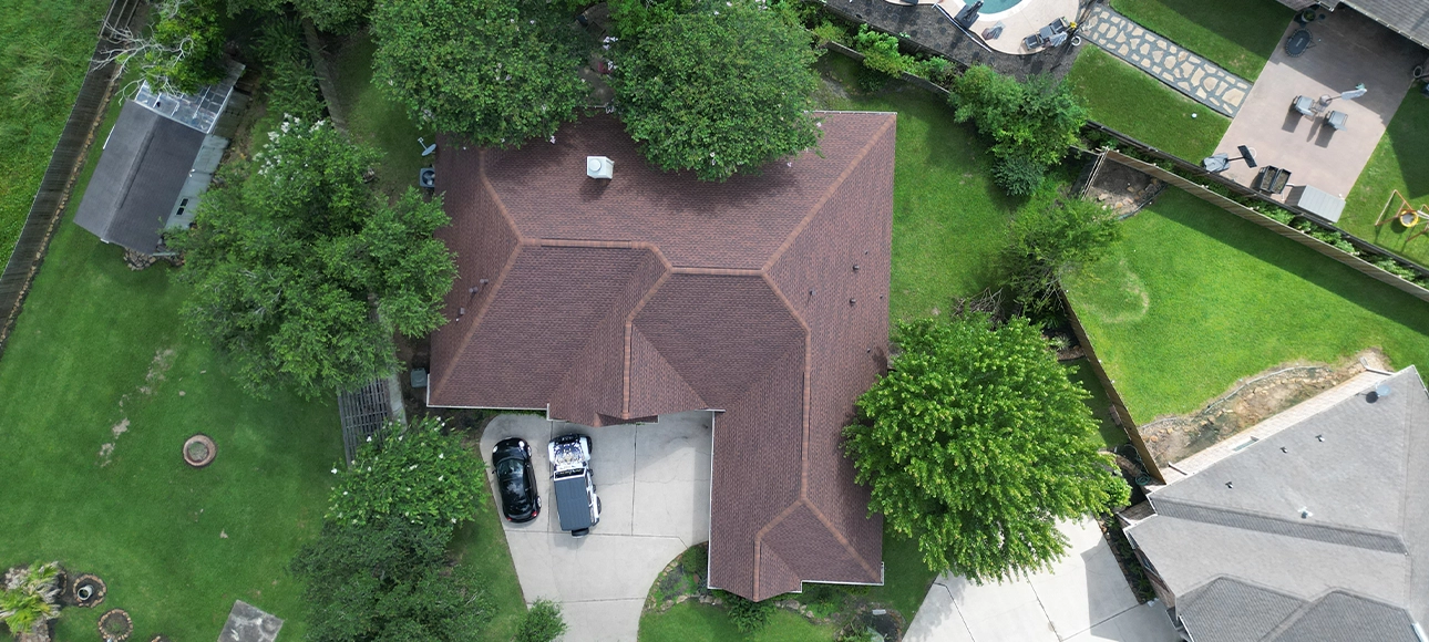 Top-down aerial view of a hip roof with new brown shingles surrounded by trees
