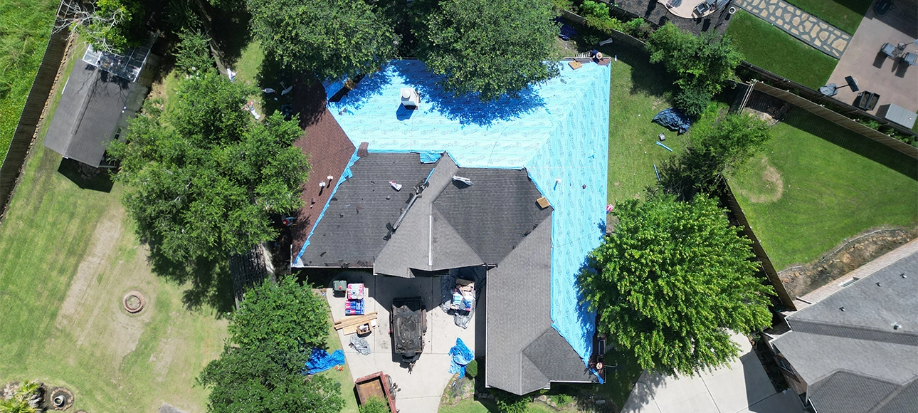 Top-down aerial view of the same roof during replacement, partly covered in blue synthetic underlayment