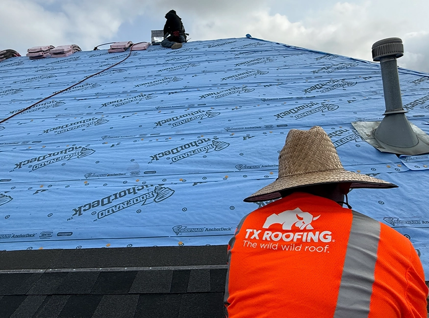TX Roofing crew member in a branded shirt and straw hat working beside new roof underlayment