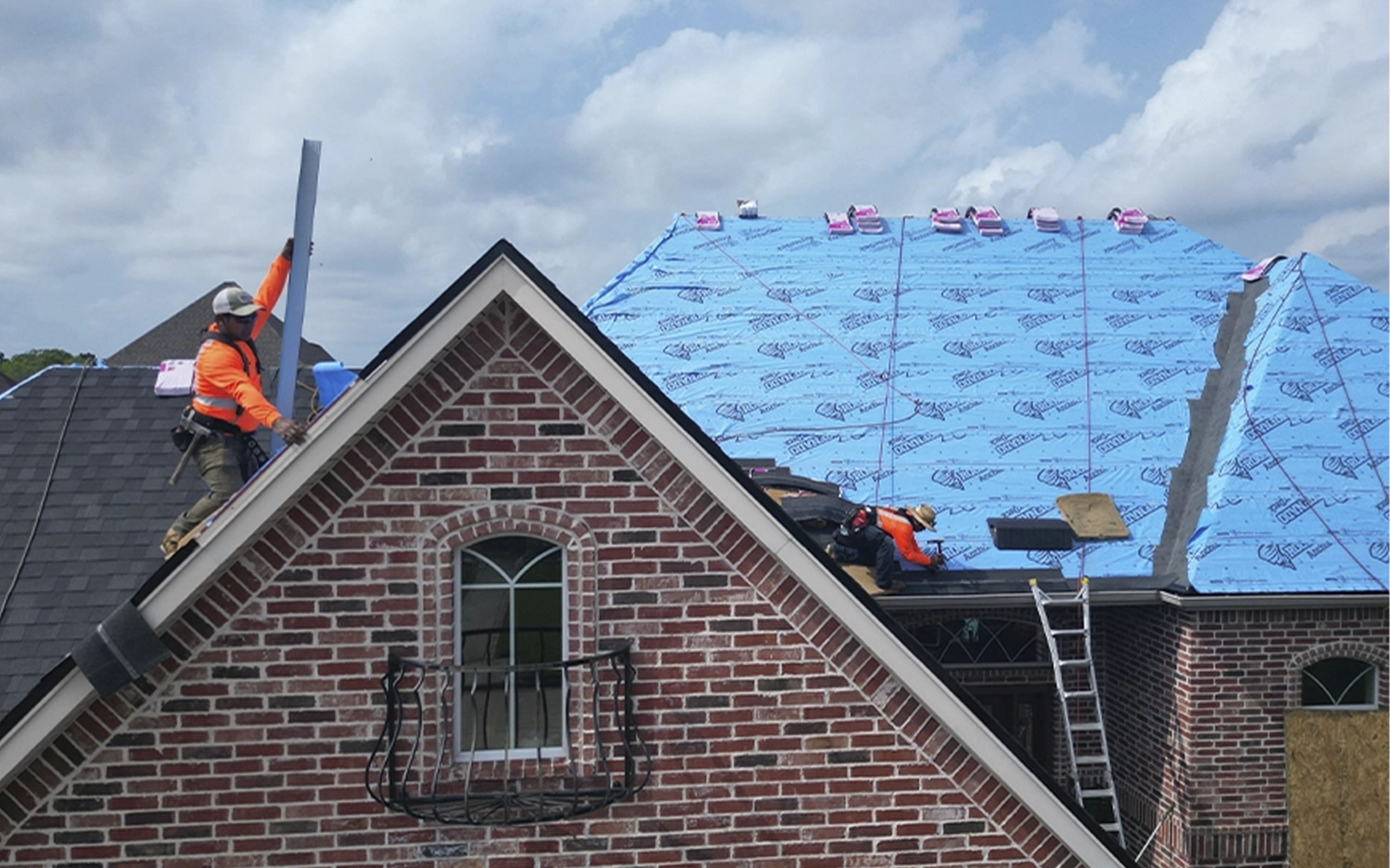 Roofers installing a ridge vent and new shingles on a two-story brick home